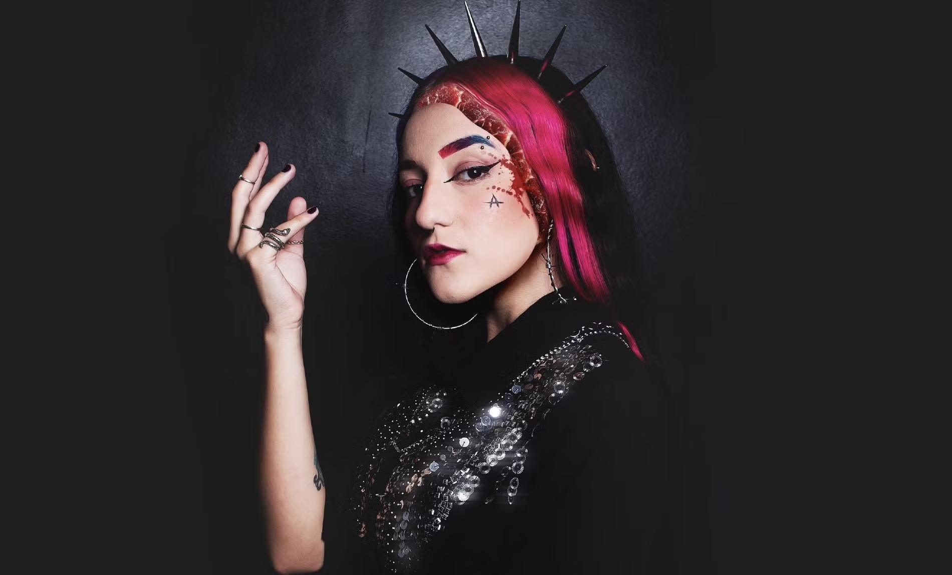 atriz ariah de cabelo rosa e roupa preta, de perfil, olhando com olhar misterioso para o lado