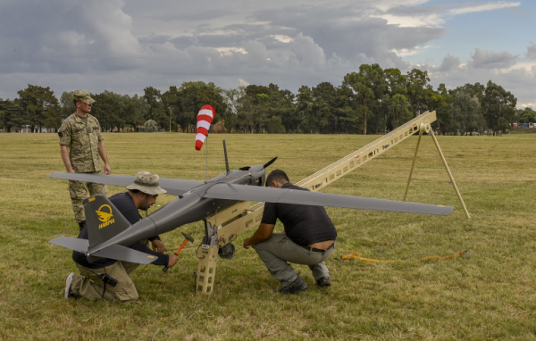 trabalhadores da ADTECH configurando equipamento similar a um planador em gramado, acompanhados por um militar fardado