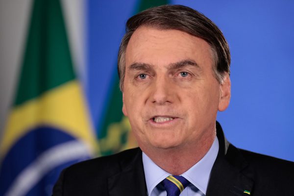 presidente jair bolsonaro em discurso em frente a bandeira do brasil usando terno