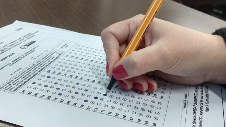 Mão de mulher segurando caneta em cima de gabarito de concurso público; prefeitura de Taubaté cancelou processos seletivos na cidade
