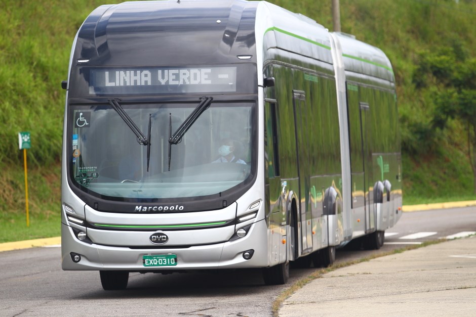 Ônibus da Linha Verde de frente, com detalhes em verde a estrada ao fundo, com vegetação.