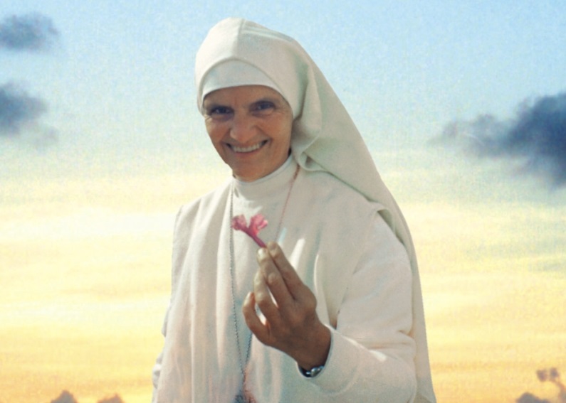 Madre Maria Teresa, fundadora do Instituto das Pequenas Missionárias, segurando uma flor, com vestimenta branca e um céu ao fundo.
