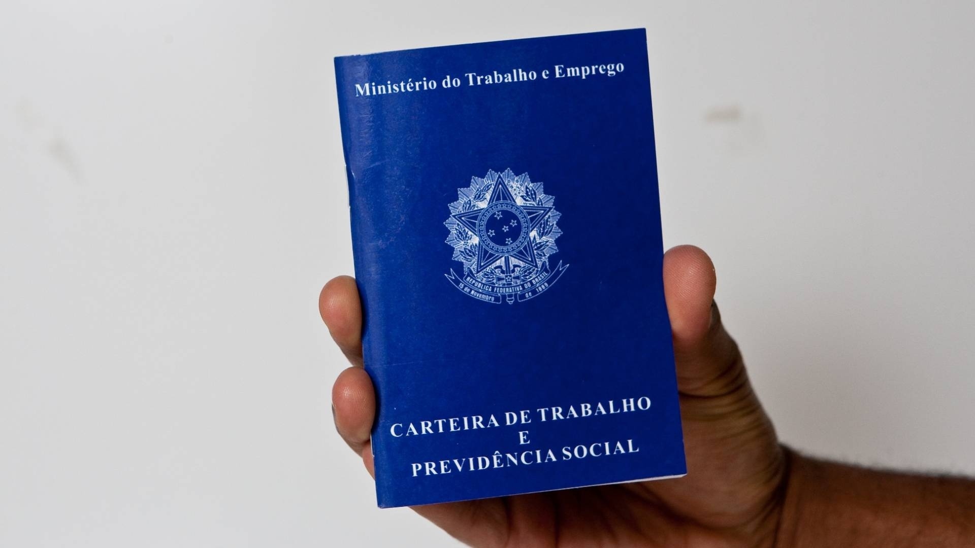 Foto ilustra a matéria sobre emprego em Ubatuba, da prorrogação do processo seletivo da Emburd, com uma mão segurando a CTPS azul.