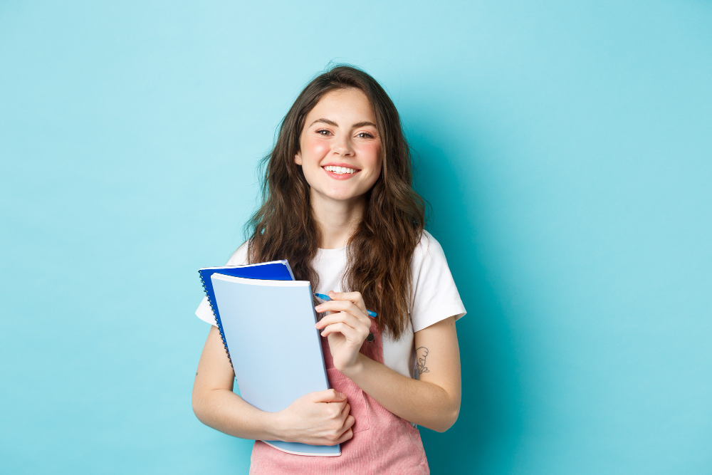 Estudante com livros e caneta na mão, sorrindo. Agência de estágios de SJC está com vagas para administração, Ensino Médio e outras áreas