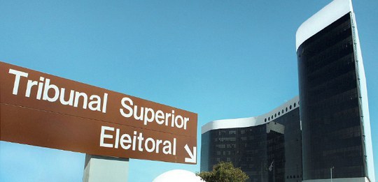 Placa apontando para a sede do Tribunal Superior Eleitoral, que determina o prazo das convenções partidárias e oficialização dos candidatos. Ao fundo, o prédio de vidro.