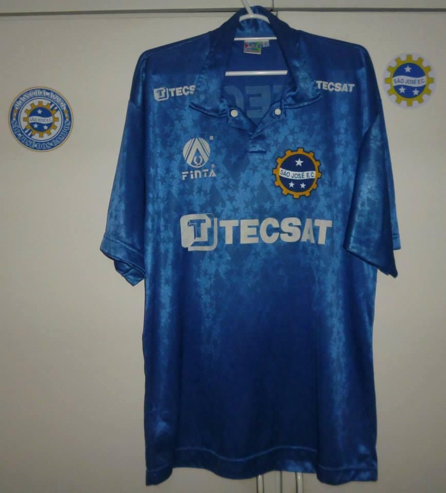 Camiseta azul anil com marcas d'água, escudo do clube e com os patrocínios da Finta e da Tecsat