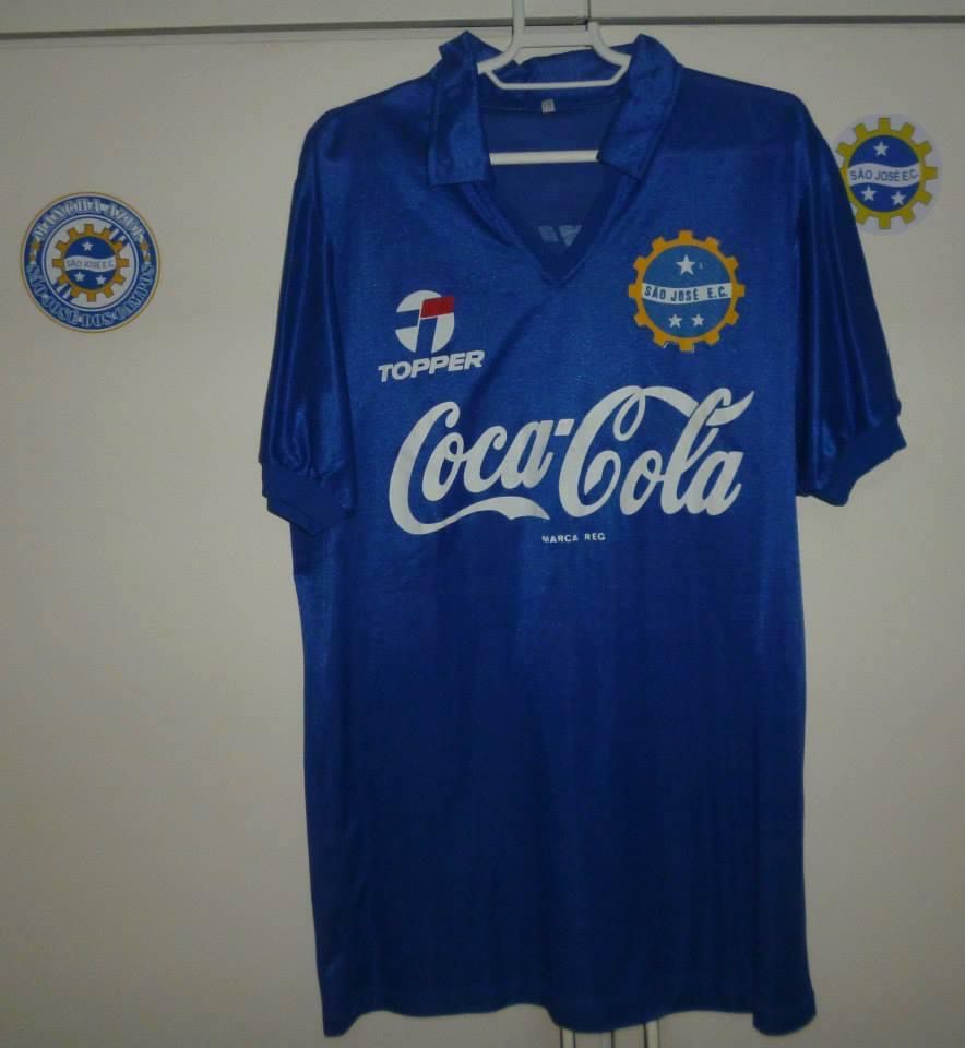 Camisa azul anil, gola polo, patrocínio da Coca Cola e do material esportivo da Topper e o brasão do clube