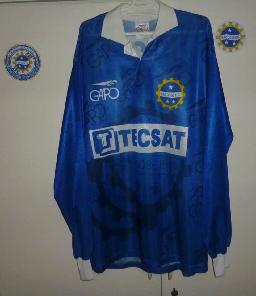 Camisa azul anil com marcas d'agua do patrocinador Gapo e do escudo do clube, com a gola e a punho branca e o patrocínio da Tecsat.