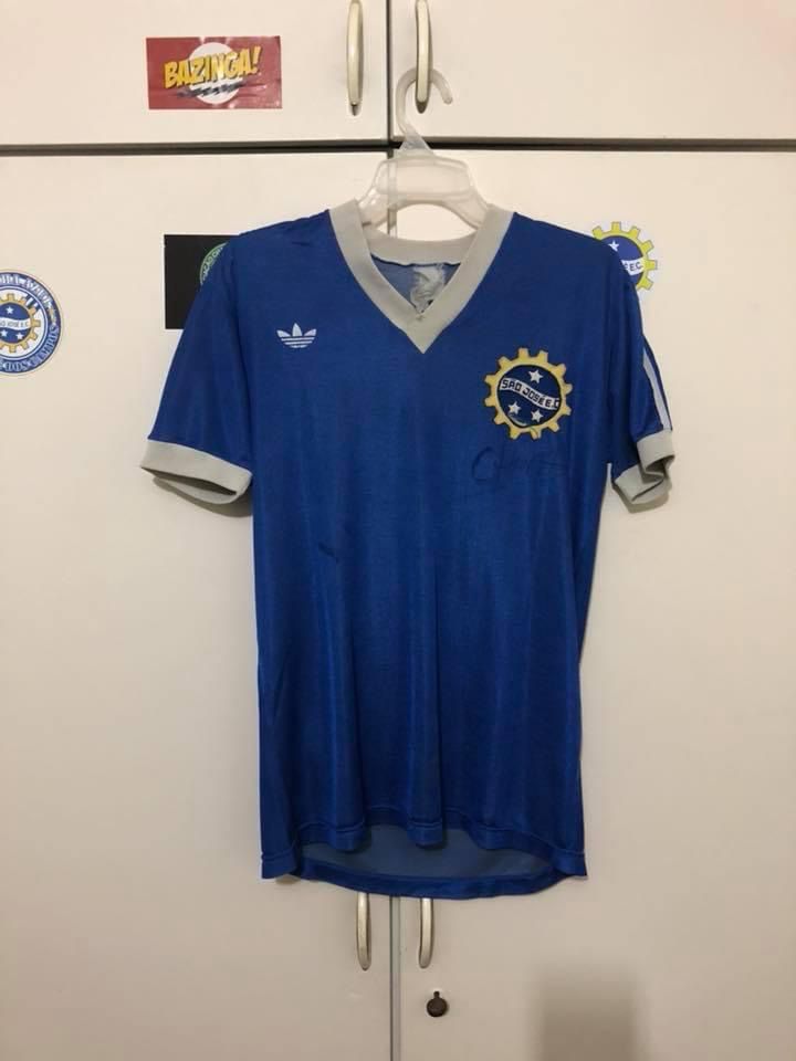 Camisa azul anil com a manga e gola nas cores brancas, escudo do São José e símbolo da Adidas na cor branca