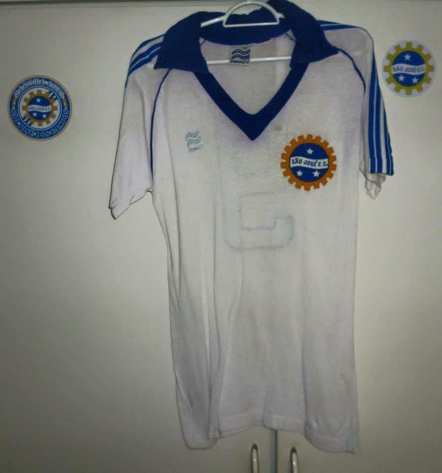 Camisa branca, com a gola azul, escudo do São José, três listras azuis nas mangas e a logo da Pênalti azul claro