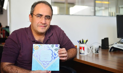 Carlos Abranches, sentado, de camisa polo roxa, sorrindo e segurando seu livro "A casa que mora em mim"