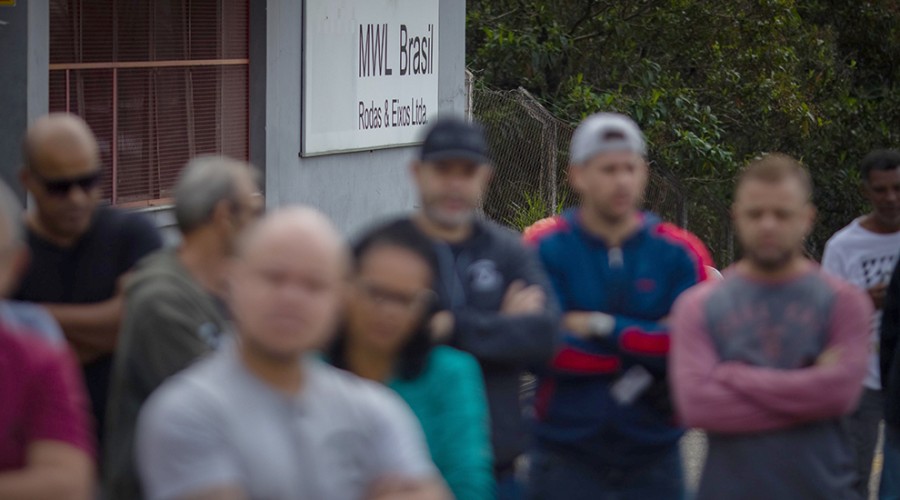 Trabalhadores, desfocados na imagem, de braços cruzados em frente a entrada da MWL em Caçapava