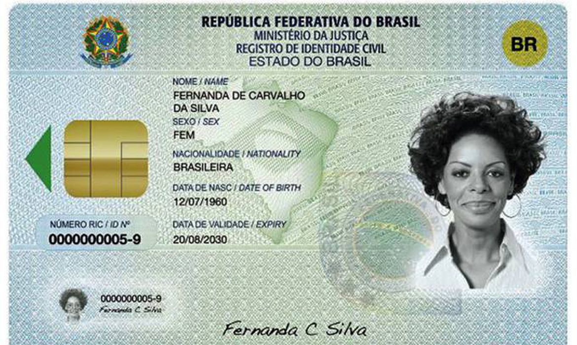Nova carteira de identidade nacional. Ela apresenta a cor azul claro nas laterais, que em direção ao meio vão se transformando em verde claro com um degradê. Sobre o verde há ainda a marca d'água de um selo da República Federativa do Brasil e um mapa do Brasil com a parte interna da bandeira nacional dentro dele. A carteira apresenta, na parte de cima e ao centro, os dizeres "República Federativa do brasil", "Ministério da Justiça", Registro de identidade Civil e "Estado do Brasil". Abaixo disso, ainda ao centro, há as seguintes informações em sequência vertical: nome, sexo, nacionalidade, data de nascimento e data de validade. Agora na parte esquerda da carteira, há um chip dourado com uma seta verde apontando para a esquerda e abaixo dele está o número da identidade. O mesmo número aparece em uma versão um pouco menor um pouco mais abaixo, no lado inferior esquerdo, junto de uma miniatura da foto da carteira. No lado esquerdo do documento, por sua vez, há a foto de identificação em preto e branco e acima dela, no canto superior direito, um selo amarelo circular com o escrito "BR" na cor preta dentro dele. Por fim, também no centro da carteira, mas na parte inferior, há a assinatura do nome do cidadão.