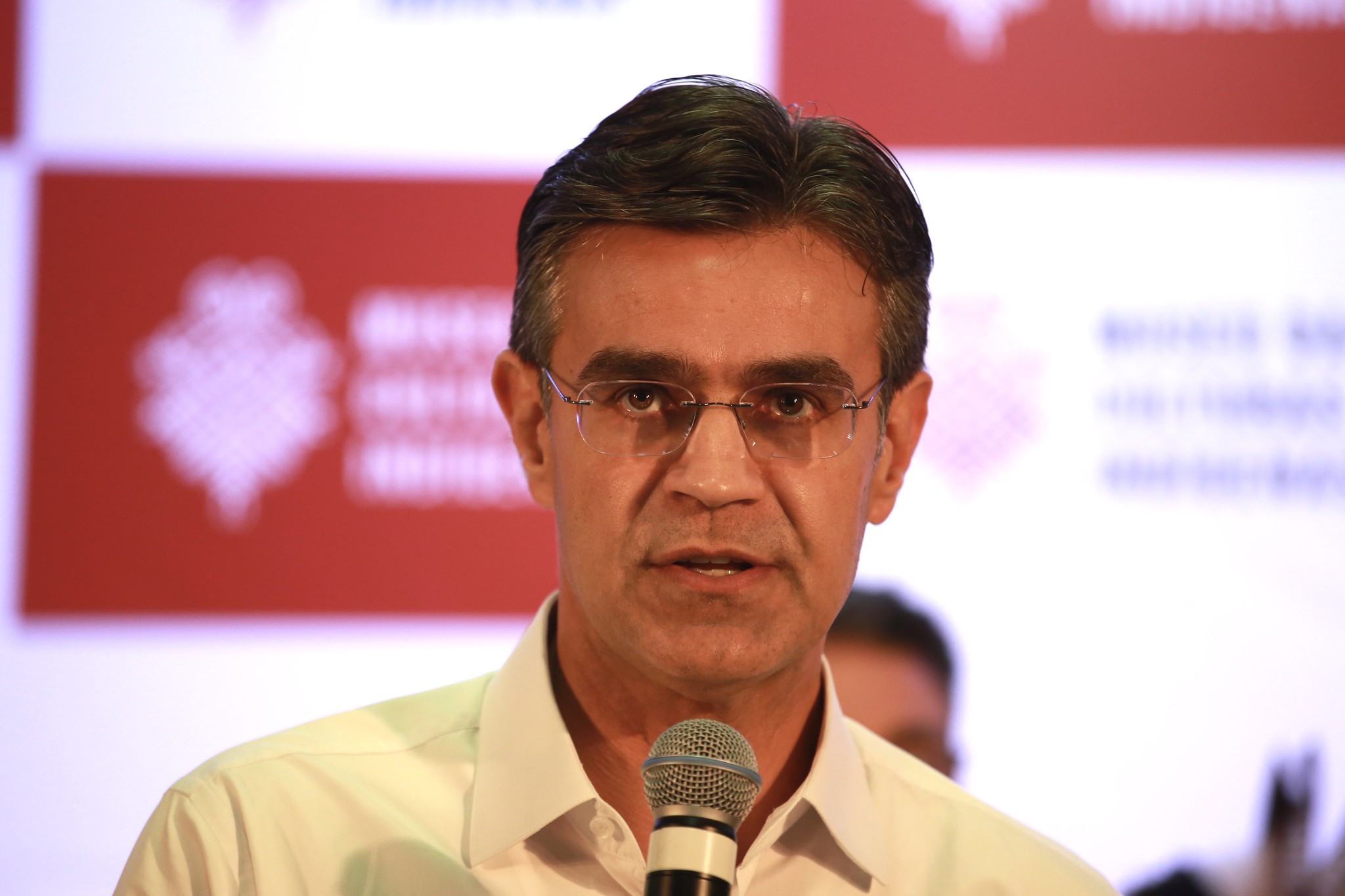 Governador de São Paulo Rodrigo Garcia em evento. Ele aparece do pescoço para cima, usa camisa branca, óculos e fala em microfone posicionado abaixo de seu queixo.