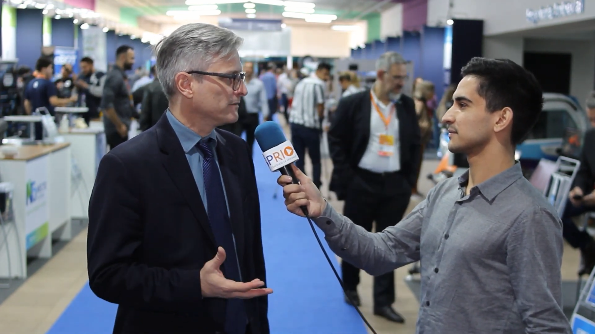 À esquerda, o diretor do Parque Tecnológico de SJC, Jeferson Cheriegate, durante entrevista ao jornalista Matheus Andrade, à direita. Cenário da PqTec Innovation Week ao fundo, com pessoas andando. - foto - sp rio mais