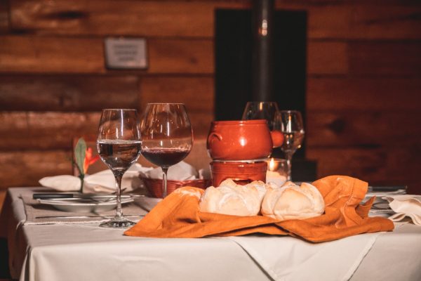 Mesa com taças de vinhos, pães e fondue.