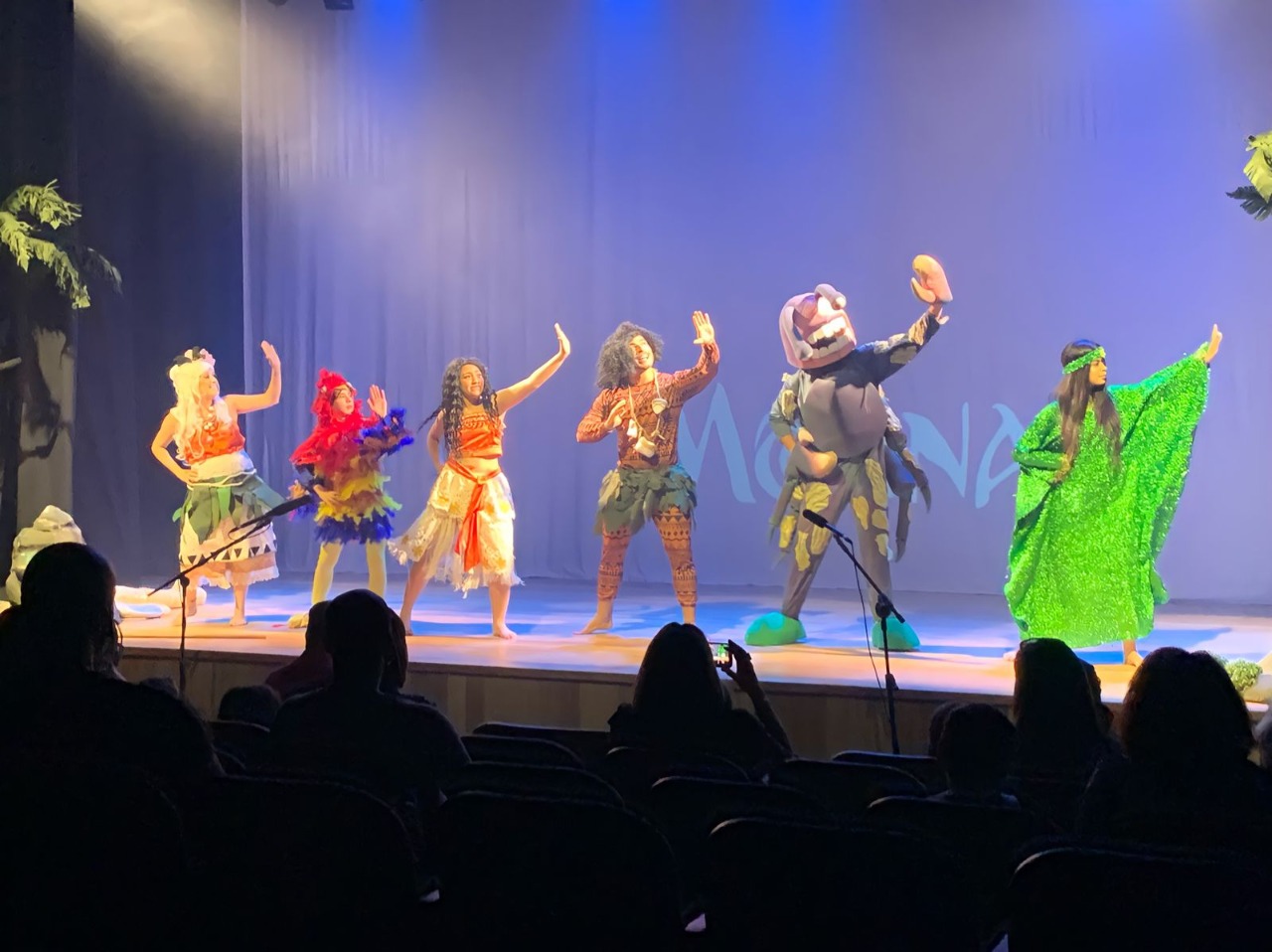 Espetáculo sendo exibido no palco do Teatro Colinas, com atores dançando e olhando para o lado direito, com fantasias.
