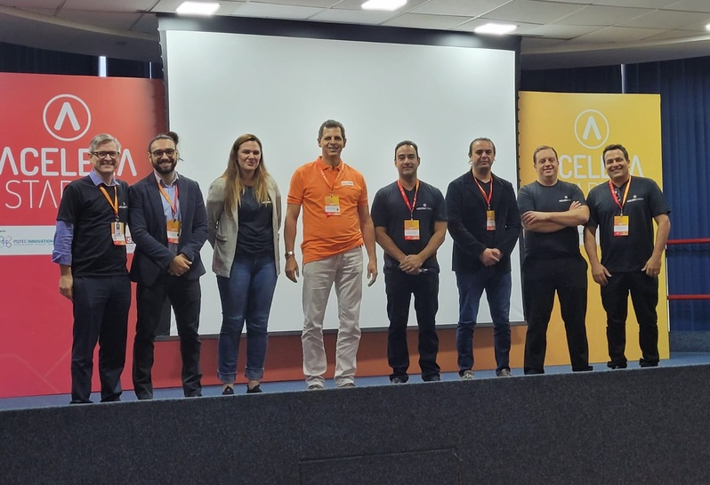 Pessoas ao lado uma das outras, em frente ao telão e ao logo da Acelera Startup, no Parque Tecnológico de SJC.