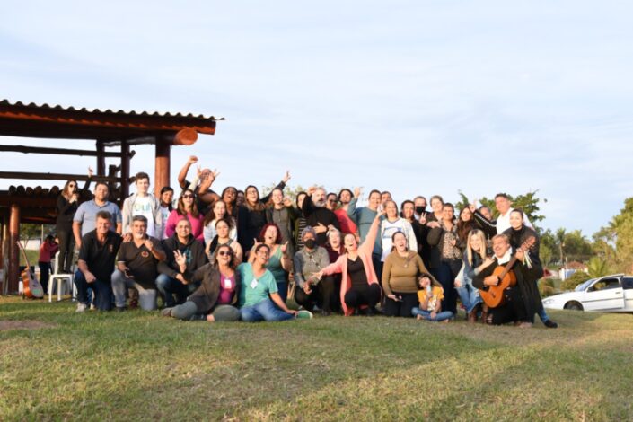 Integrantes da Feira Cultural TuduJuntu, que será realziada em Caçapava em setembro, reunidos e com os braços para o alto, em uma área verde.