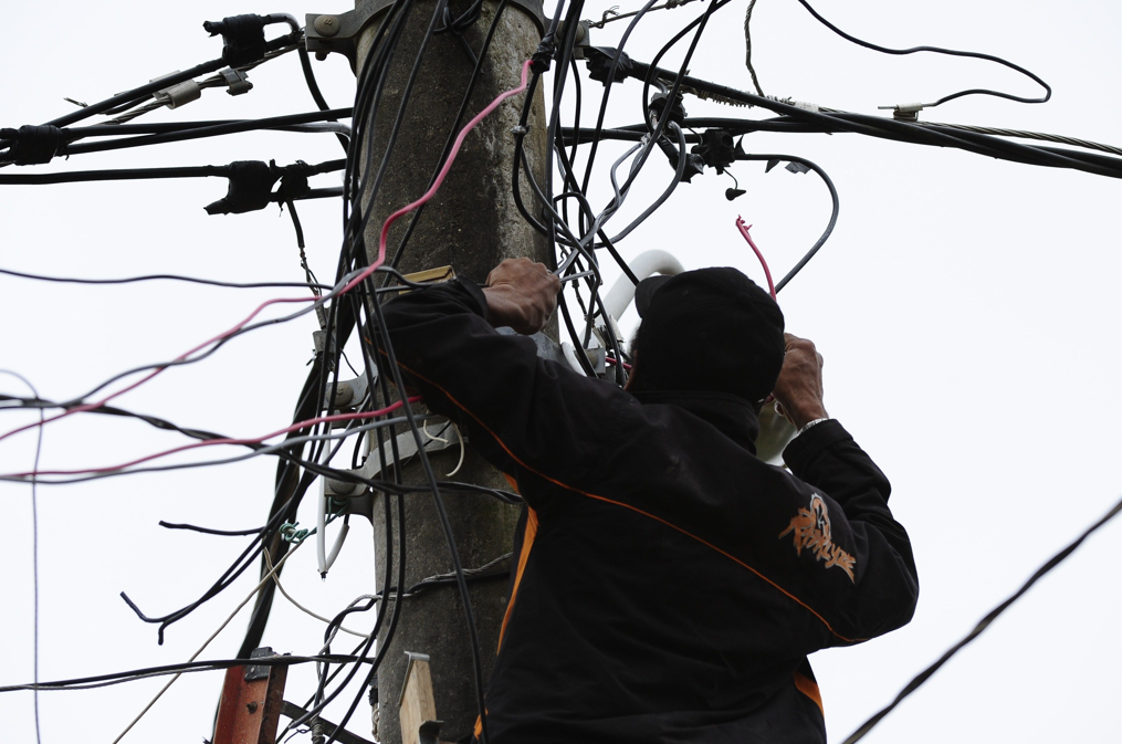 Pessoa subindo em um posto, realizando um gato de energia elétrica com os fios.