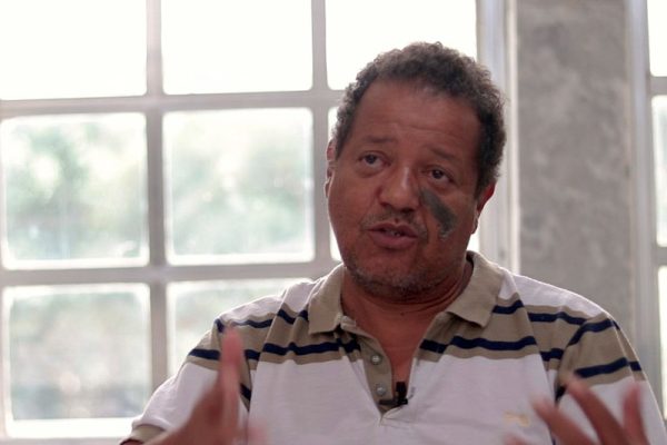 Candidato Luiz Carlos Prates. Ele é pardo, possui cabelo crespo, barba por fazer e mancha de nascença no lado esquerdo do rosto.