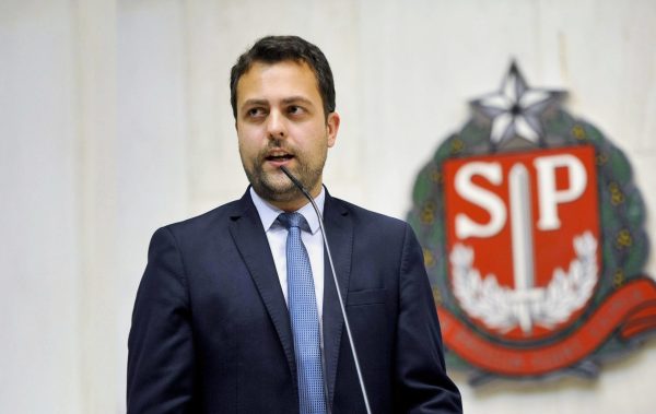 Candidato Ricardo Mellião. Ele é branco, possui cabelo liso castanho escuro e barba por fazer.