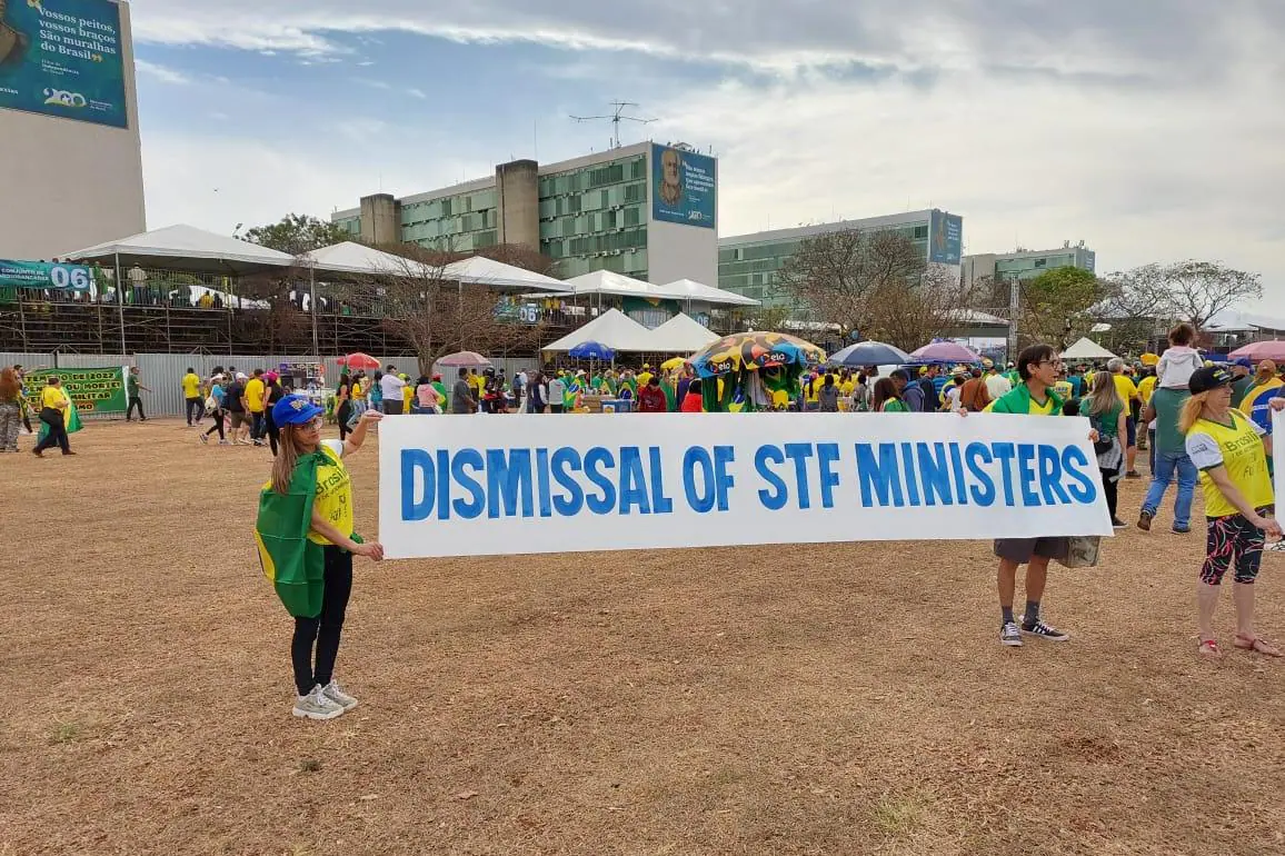 Pessoas com a roupa do Brasil, segurando um cartaz em inglês que pede a demissão dos ministros do STF, em escrita em azul.