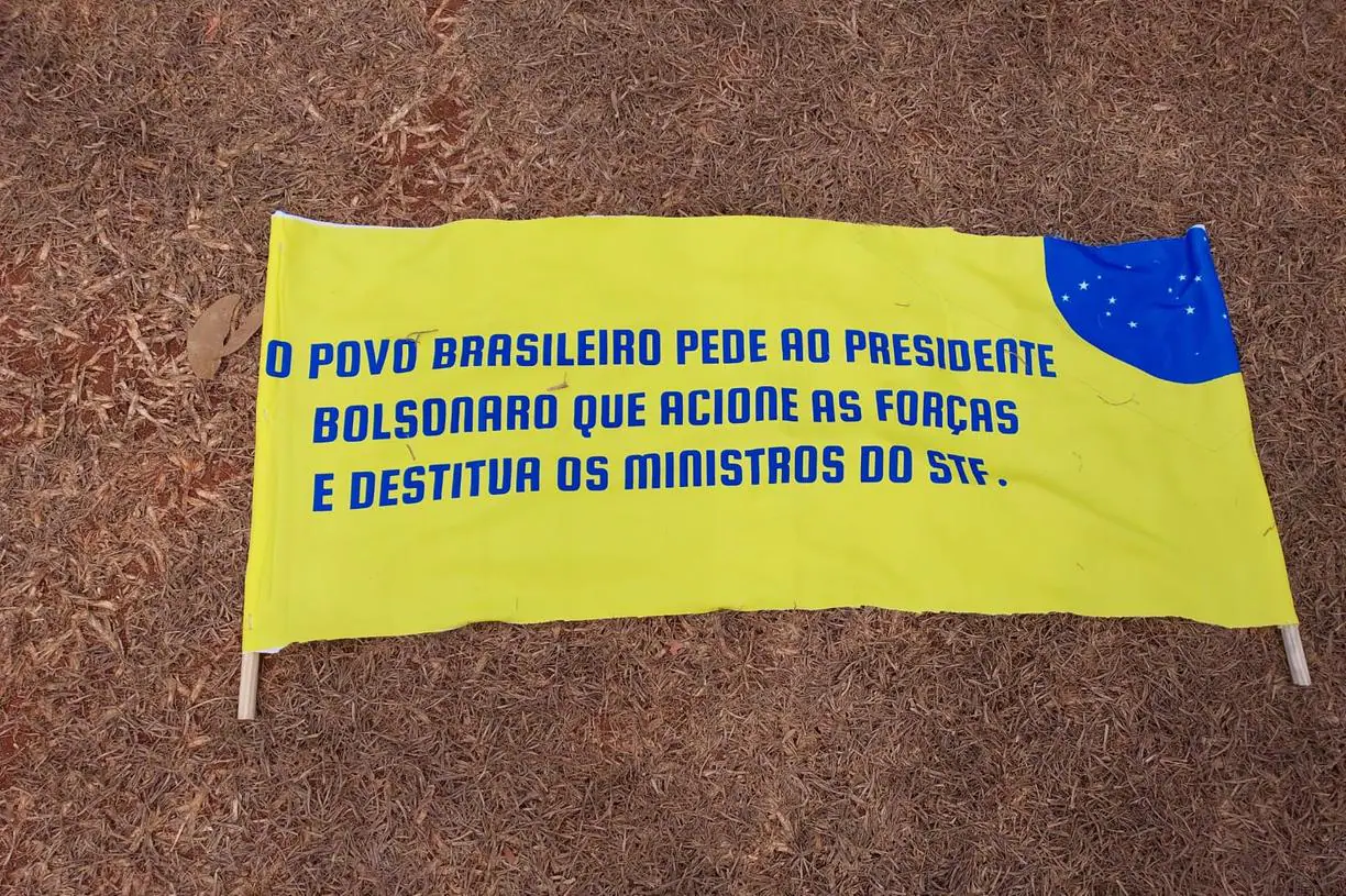 Cartaz em amarelo, no chão, com letras em azul, pedindo intervenção militar ao presidente Bolsonaro.