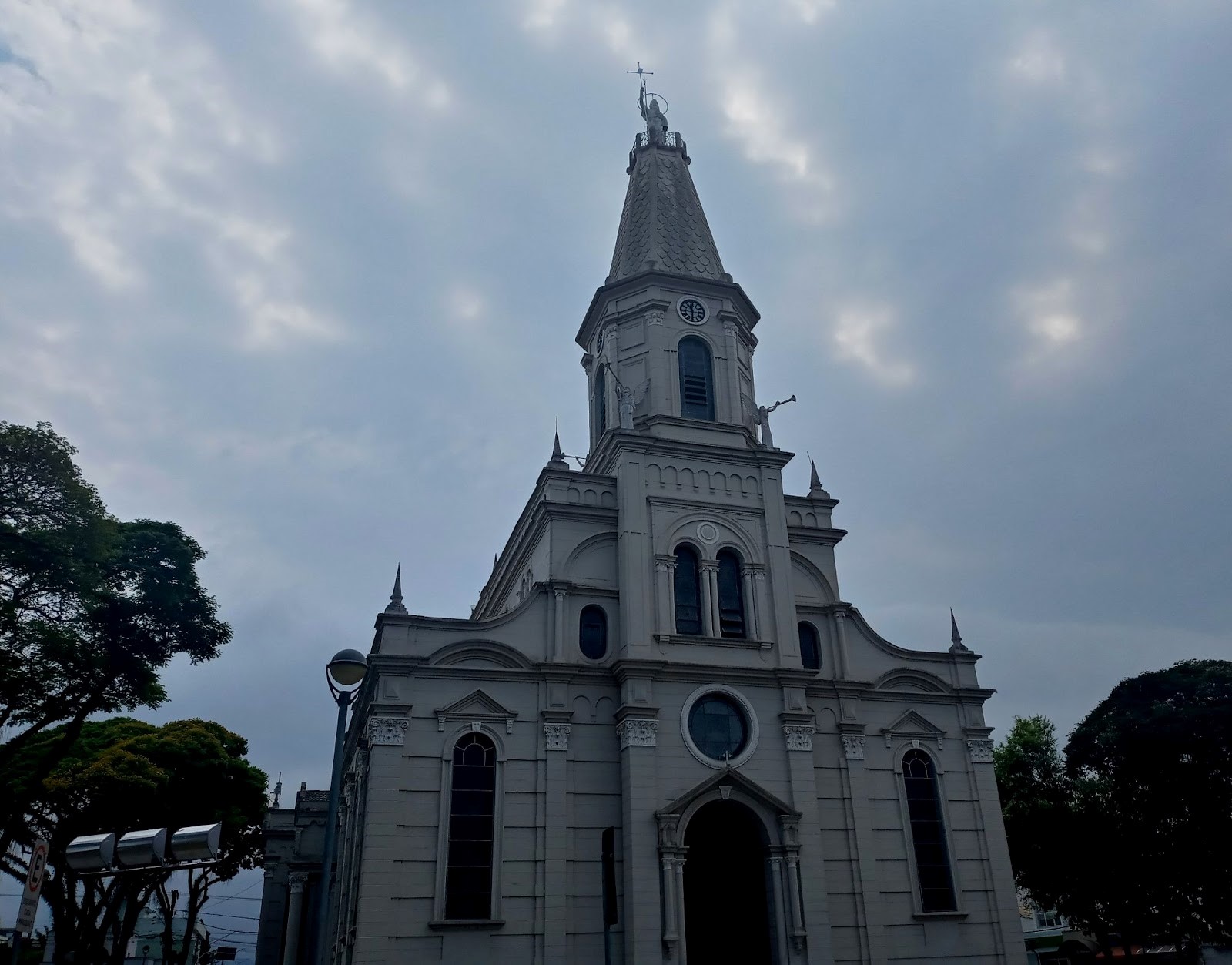 Fachada da Igreja Matriz de São João Batista, um dos pontos turísticos de Caçapava, com um céu azul, árvores na laterais e a fachada branca em destaque, vista de baixo para cima.