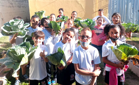 alunos de escola municipal com a colheita do projeto Mãos à Horta