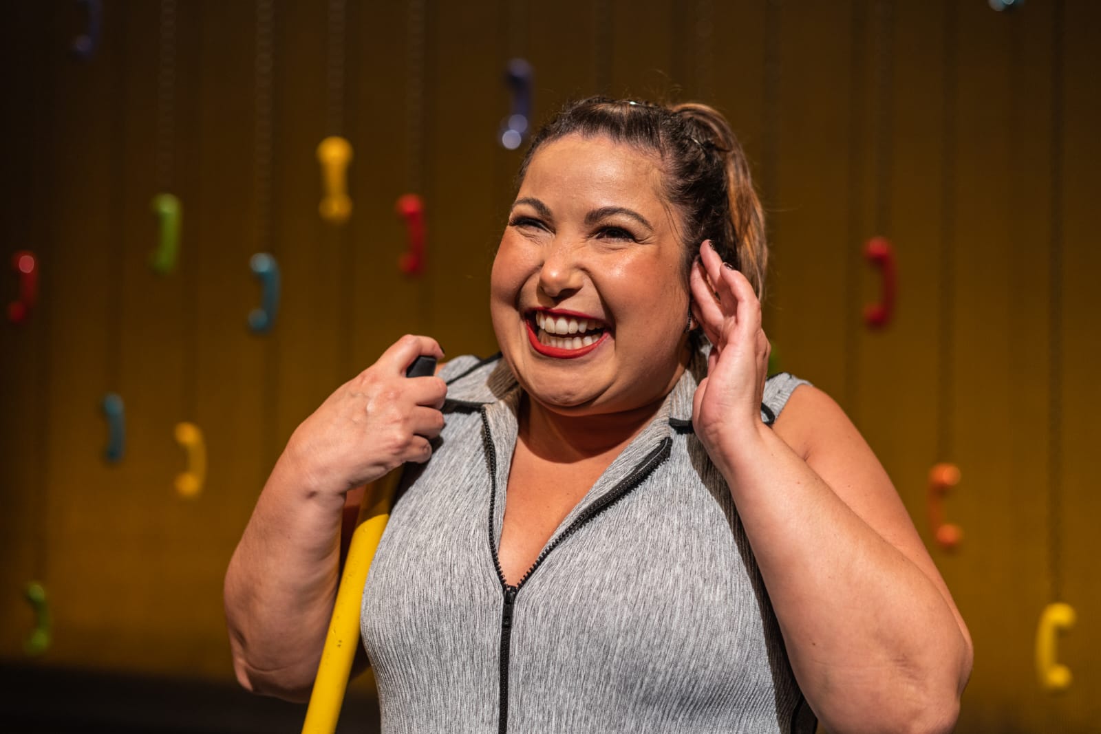 Atriz Mariana Xavier, sorrindo para a câmera, com a mão na orelha, durante espetáculo teatral. Ela é a atração de São José dos Campos neste fim de semana.