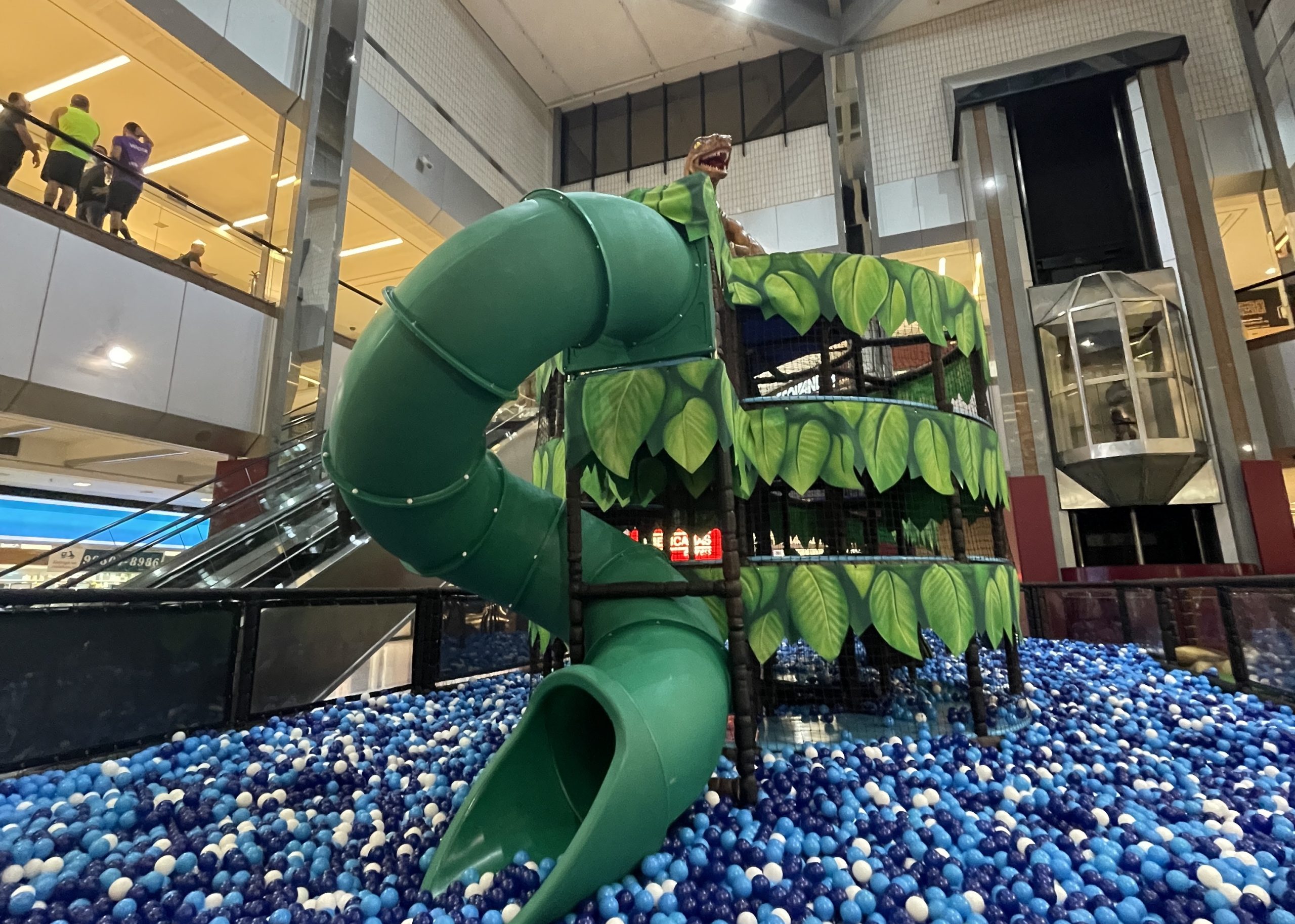 Brinquedo Mundo das Bolinhas, ou Dino Adventure, localizado no Colinas Shopping, com bolinhas azuis no chão, um escorregador verde no meio e a estrutura do shopping em volta.