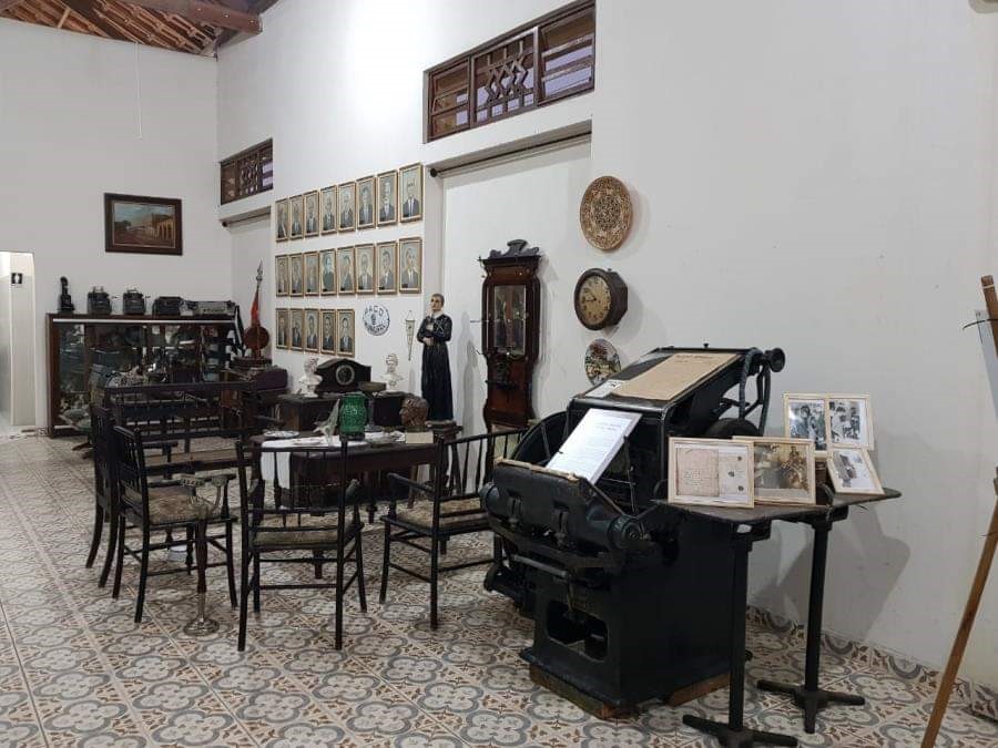 Parte interna do Museu José de Moura Resende, em Caçapava, com um chão de piso, parede branca e móveis antigos, em diversas cores.