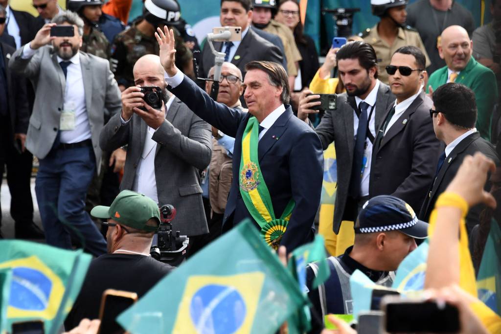 Bolsonaro com a faixa presidenciável verde e amarela, no meio das pessoas, acenando para o público.