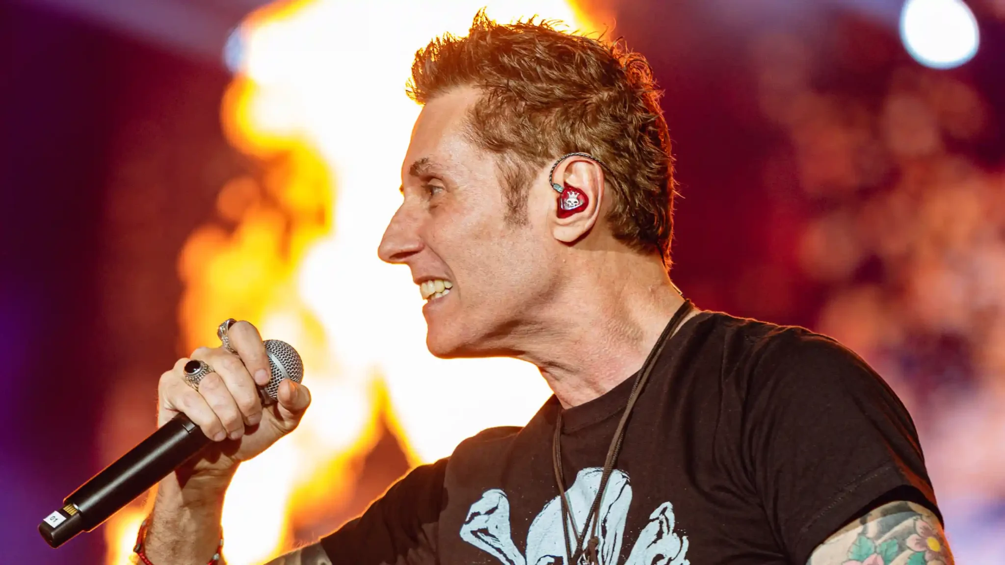 Dinho Ouro Preto durante apresentação no Rock in Rio, com um fundo de fogo, segurando o microfone com uma camiseta preta.