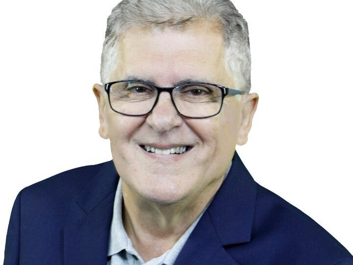 Claudio Miranda, candidato a deputado federal por Lorena posando sorrindo para foto. Ele é branco, idoso, tem cabelo curto branco, usa óculos e veste camisa social azul clara e blazer azul marinho.