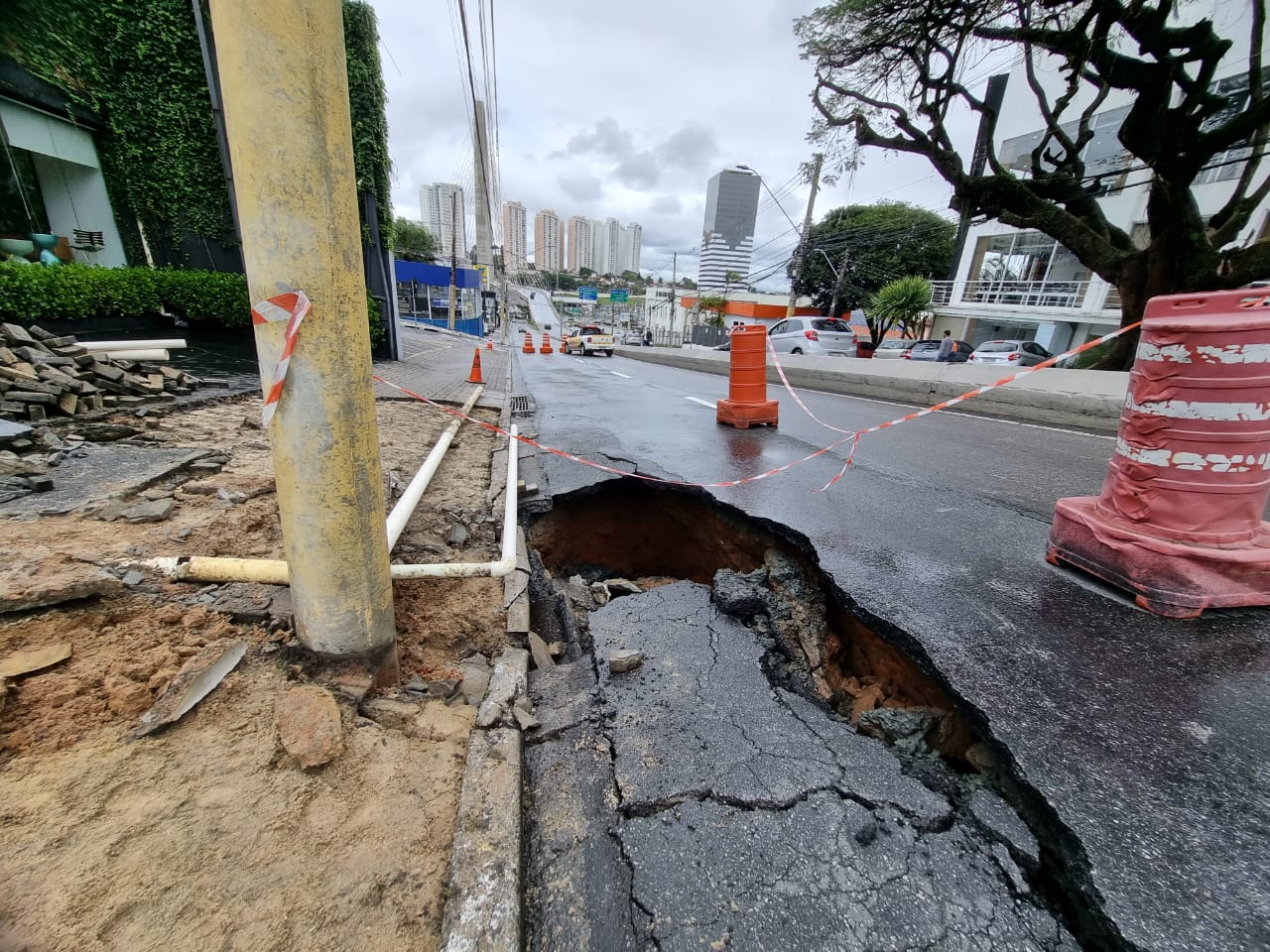 Cratera em SJC (São José dos Campos), no Jardim Colinas, com faixas de interdição e a cidade ao fundo.