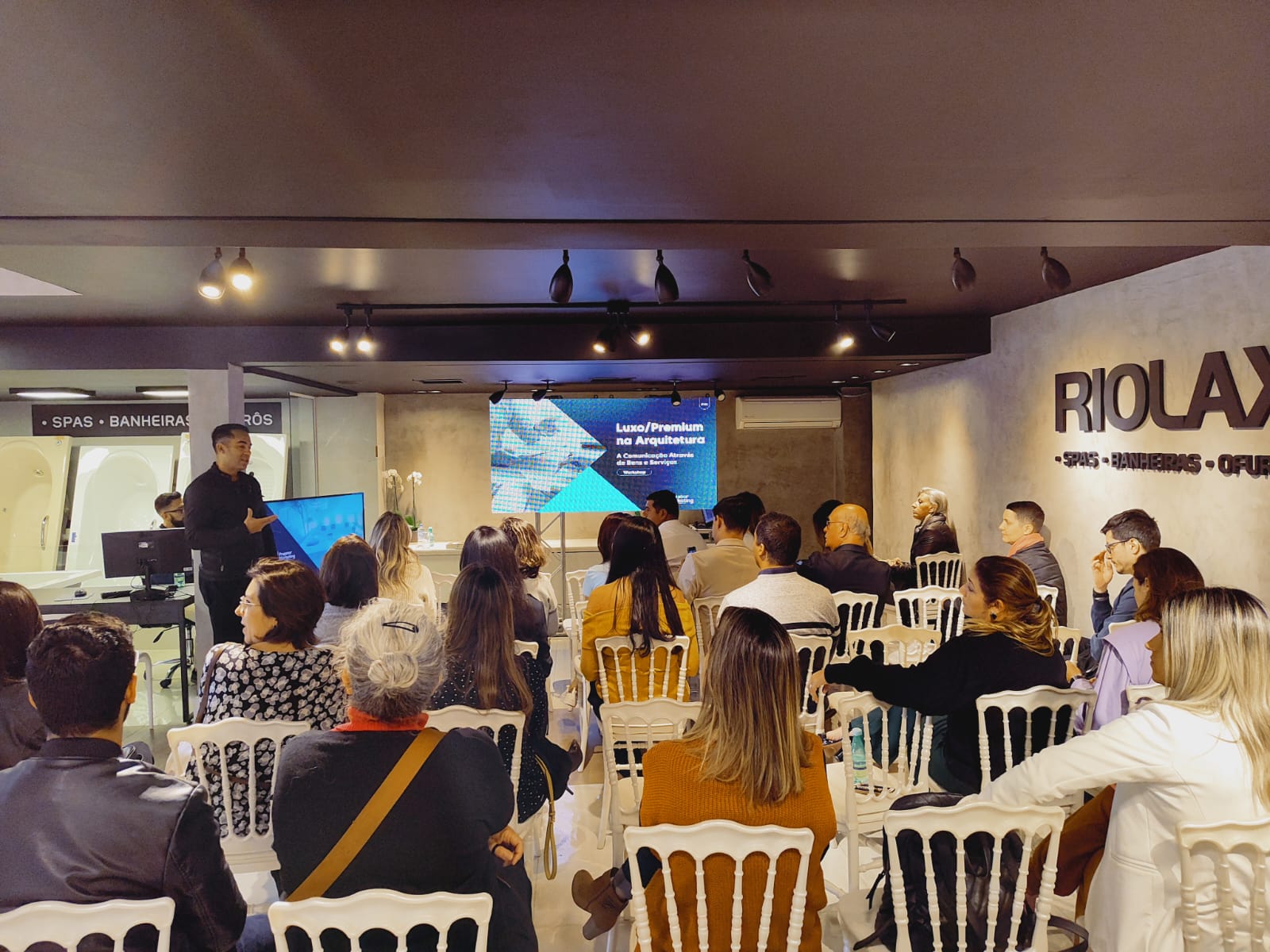 Pessoas sentadas em cadeiras de frente para o telão que passa o slide do Workshop.