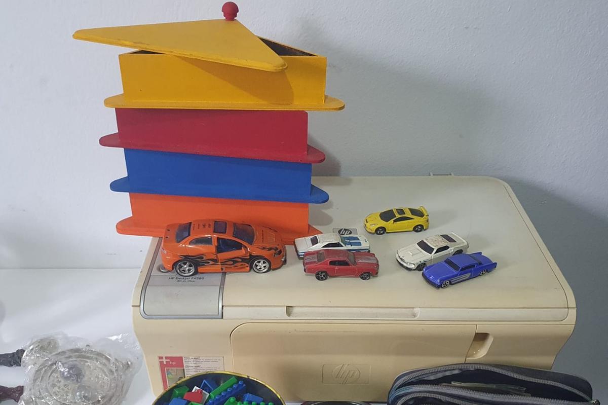 Brinquedos em cima de uma impressora, como carrinhos e objetos coloridos, com uma parece funda ao branco, na casa do homem que foi preso por suspeita de pedofilia infantil em São José dos Campos.