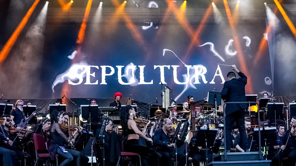 Banda Sepultura no telão, com integrantes tocando instrumentos, em um fundo preto.