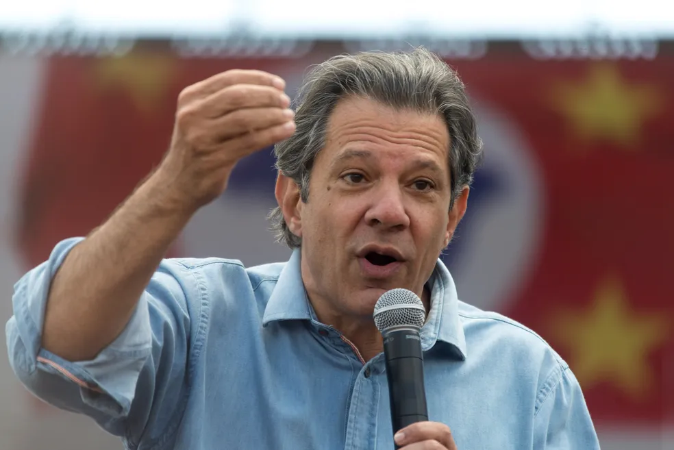 Em Suzano, Haddad promete aumentar orçamento da cultura; na foto ele fala no microfone, com a bandeira de São Paulo ao fundo e uma camisa azul