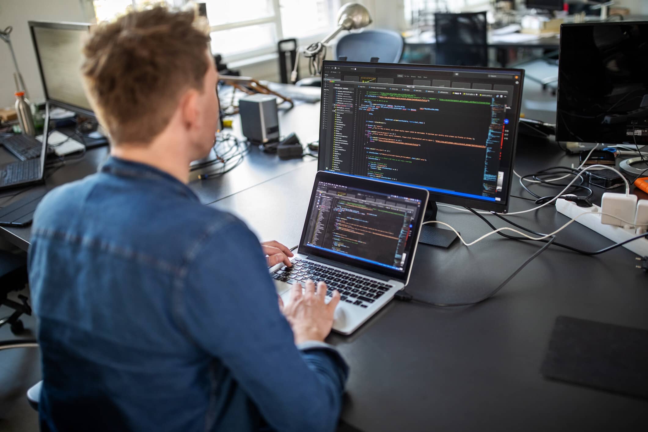 Homem trabalhando em um notebook, com um monitor ao lado, com uma camisa azul, em cima de uma mesa preta, simulando as vagas de emprego na Dataside, startup de São José dos Campos