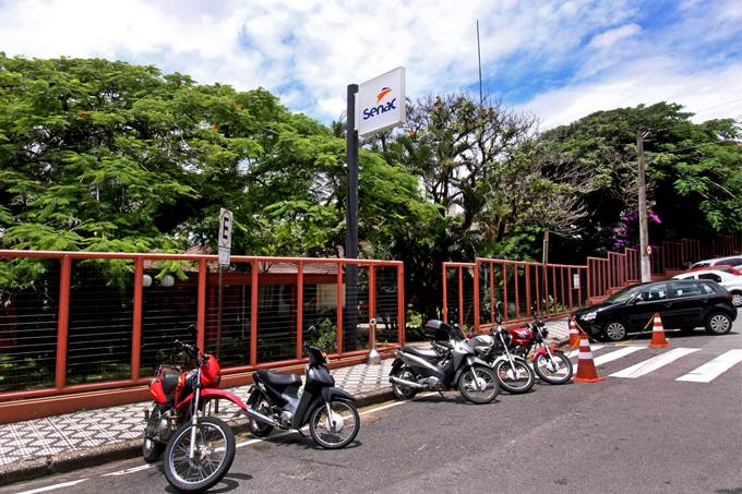 Fachada do Senac Taubaté, onde uma aluna agrediu uma colega com uma faca, após discussão política. Foto mostra fachada da escola, com árvores em volta e motos estacionadas na frente.