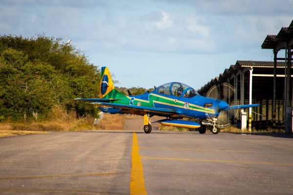 aeronave A-29, da esquadrilha da fumaça, em solo. Avião tem as cores da bandeira do Brasil, azul, verde e amarelo.