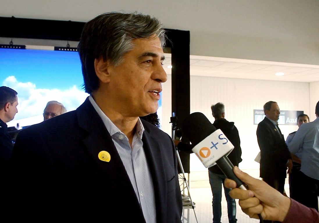 Eduardo Azevedo do Vale durante entrevista à SP RIO+, com terno preto, falando ao microfone, durante evento no aeroporto de SJC.