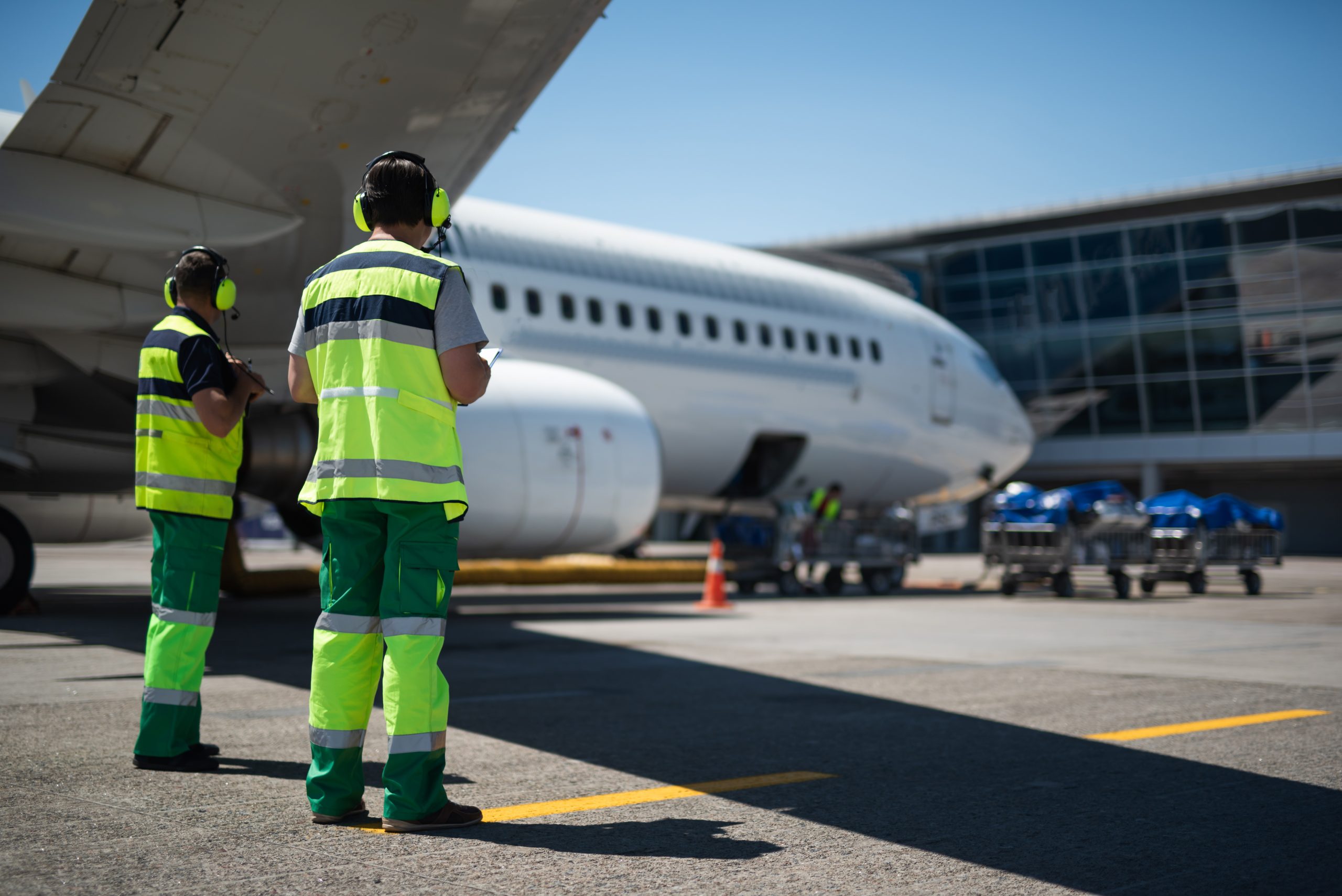 Foto mostra duas pessoas com roupas verde, em pé, ao lado uma da outra, olhando para um avião da Embraer, que, junto com a Aero-Masters, assinou um acordo comercial para uso da plataforma Beacon.