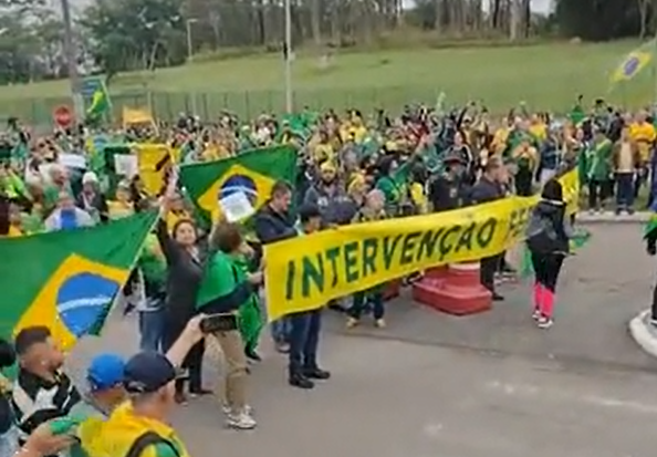Foto mostra manifestantes com as cores do Brasil, segurando um cartaz pedindo intervenção militar, em frente ao DCTA, em SJC (São José dos Campos).