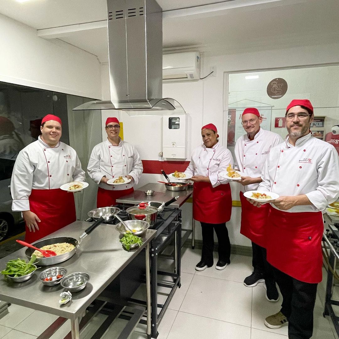 Alunos da Escola de Gastronomia Chef Gourmet Taubaté, em uma cozinha, pratos no balcão e alunos com roupas vermelhas.