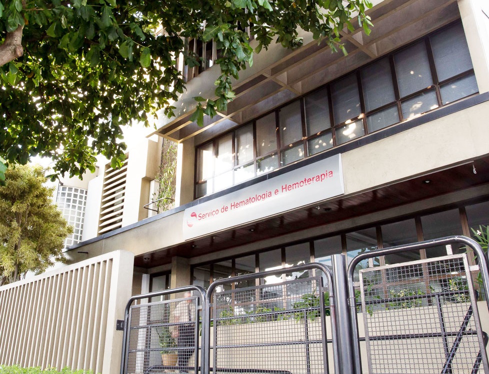 Fachada do Serviço de Hematologia e Hemoterapia, do Banco de Sangue de SJC, com uma árvore em cima e grades ao redor.