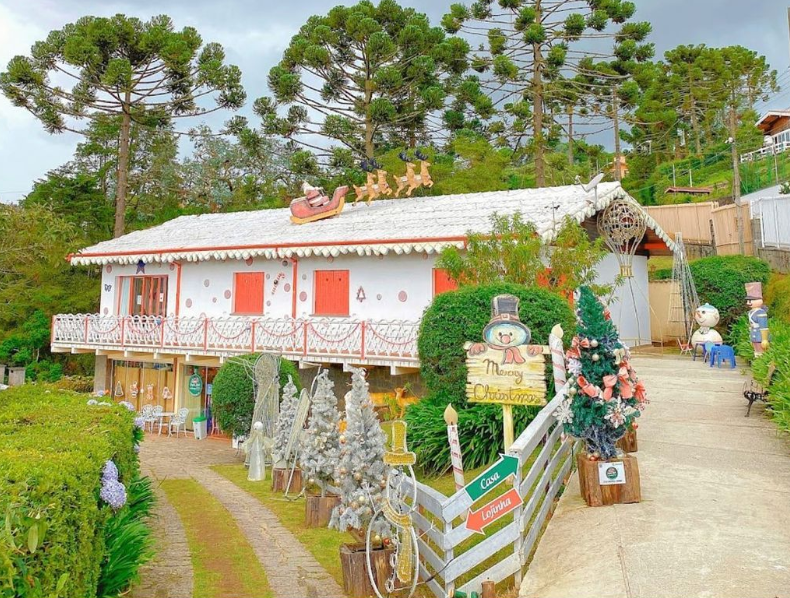 Casa do Papai Noel na montanha durante o dia, com árvores ao fundo e decorações natalinas.